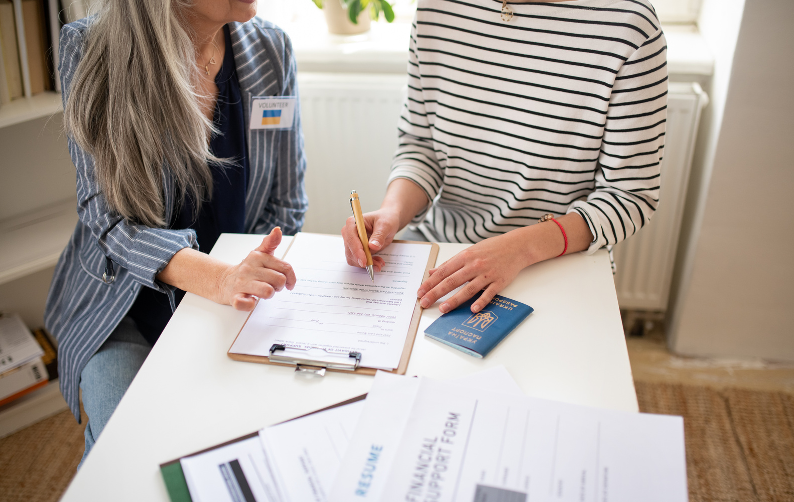 Senior Woman Volunteer Helping Ukrainian Woman to Fill in Forms at Asylum Centre.