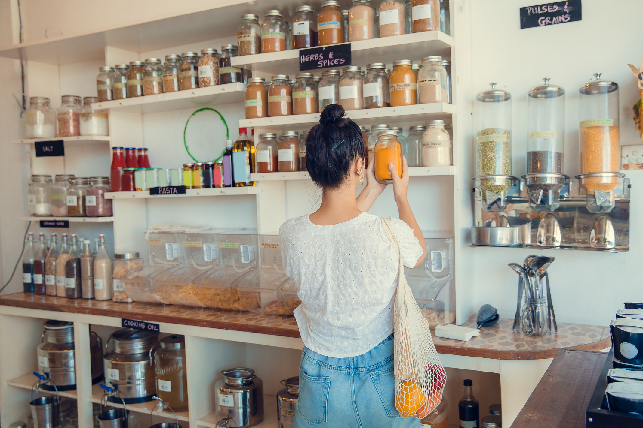 Young woman shopping in zero waste plastic free store with reusable mesh bag. Low waste lifestyle. Sustainable eco lifestyle